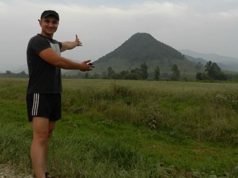 Person standing in a grassy field with a mountain in the background